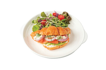 Croissant sandwich with salmon on white plate, served with fresh salad leaves.