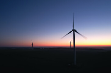 Obraz premium Three rotating silhouettes of wind turbine propellers against the backdrop of the night sky. Sustainable production of electricity from wind energy. Renewable energy concept.