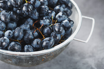 Ripe black grapes in a metal bowl on a black background.