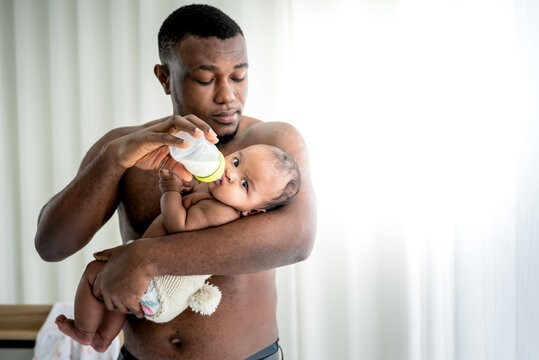 Blurred soft of African father feeding milk from bottle milk to his baby newborn daughter, to African family and food for infant concept. This picture focuses on baby