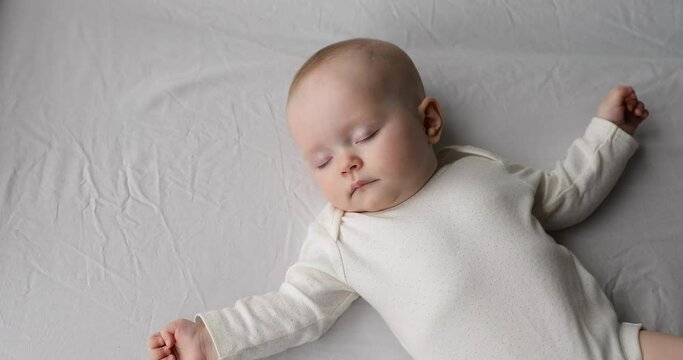 Sleeping like a newborn. Healthy happy little infant relax on big cozy bed nap alone spreading tiny hands wide. Cute funny baby dreaming well in comfy clothes enjoy safety comfort silence at bedroom