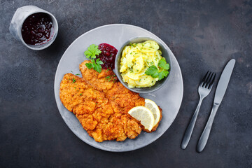 Traditional deep-fried schnitzel with potato salad, cranberries and lemon slices served as top view...
