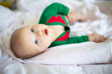 Cute caucasian baby girl six months old wearing elf costume green color. Adorable Santa helper lying on bed at home on white background