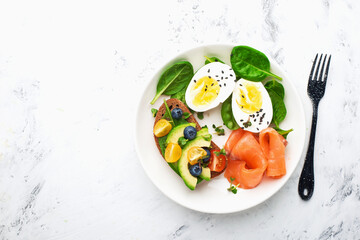 Delicious breakfast, tapas, appetizer. Bread, vegetables, herbs, spinach, eggs, salmon, berries, blueberries. Top view.