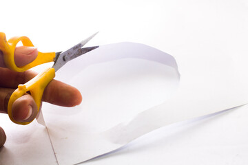 cut white paper using yellow scissors on an isolated white background. South Kalimantan, Indonesia. Dec 12, 2021. 