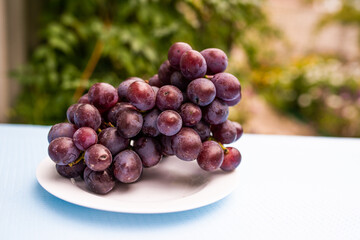 Ripe blue grape berries cluster on plate standing on table