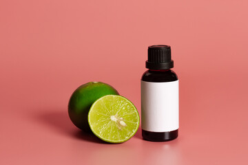 Bottle with blank label mock-Up and fresh lime on pink background. Essential oil concept.