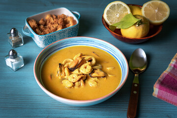 Seafood soup, based on prawns, mussels, clams, hake and squid, accompanied with pieces of fried bread, on a light blue wooden table.