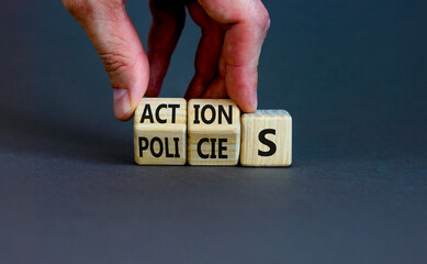 Actions and policies symbol. Businessman turns wooden cubes and changes the word policies to action. Beautiful grey table, grey background, copy space. Business actions and policies concept.