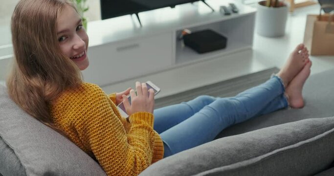 Portrait preteen girl using mobile phone and relaxing on the couch. She is online. Dolly shot
