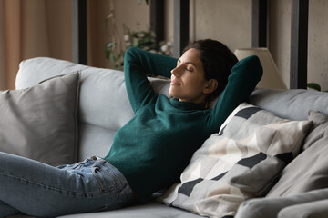 Happy calm Hispanic young woman sit relax on cozy sofa in living room dream or take nap at home. Peaceful millennial Latino female rest on couch sleep, relieve negative emotions. Peace concept. - obrazy, fototapety, plakaty