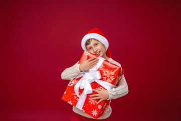 Happy laughing boy in Santa hat with Christmas gift on red background. the child is happy and holds a big gift in his hands. New year sales, advertising, discounts. Copy space.