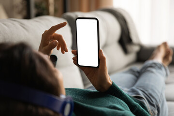 Close up back view of Latin woman lying on couch use modern cellphone with white mockup screen....
