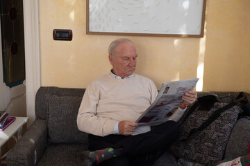 bellissimo nonno dai capelli bianchi che legge il quotidiano sul divano di casa - obrazy, fototapety, plakaty