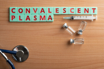 Convalescent plasma written with red and green tiles on a wooden table along with some vials a...
