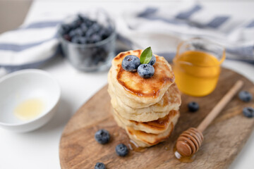 Blueberry pancakes served with honey syrup and fresh blueberries on wood on a light background, copy space. Homemade breakfast.