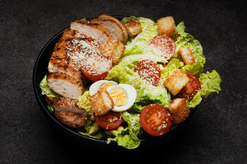 Caesar salad with chicken breast, cherry tomatoes and parmesan on a dark background