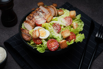 Caesar salad with chicken breast, cherry tomatoes and parmesan on a dark background