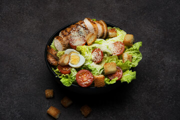 Caesar salad with chicken breast, cherry tomatoes and parmesan on a dark background