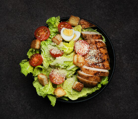Caesar salad with chicken breast, cherry tomatoes and parmesan on a dark background
