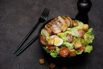 Caesar salad with chicken breast, cherry tomatoes and parmesan on a dark background