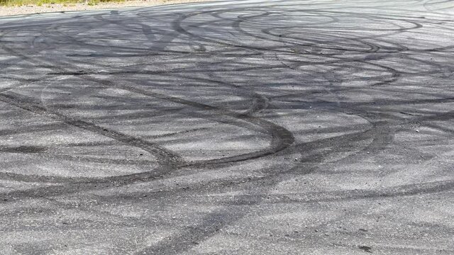 A wide view showing a road filled with skid marks, with trees and blue sky in the background, and then zooms in to focus on just the densest part of the skid marks.