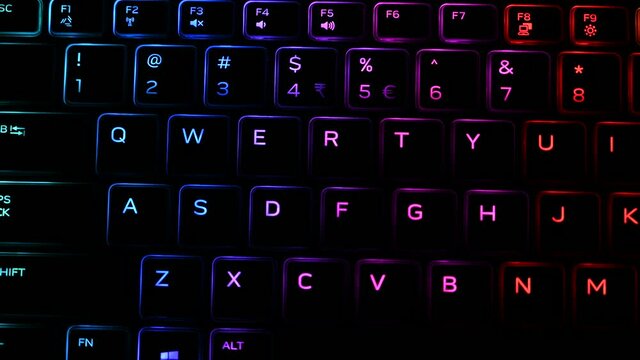 Keyboard with RGB backlit illumination changing colors for virtual video games and editing on powerful Computer in dark office room. Rainbow spectrum in modern technology.