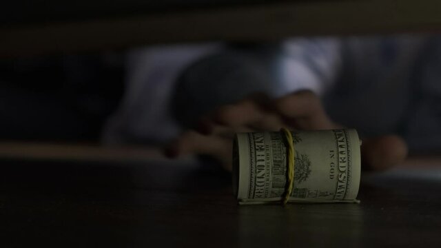 A man pulls out hidden dollars from under the bed, close-up