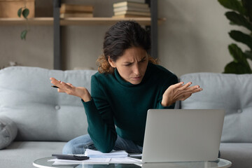 Unhappy Latino woman look at laptop screen frustrated by bankruptcy or debt paying online on...