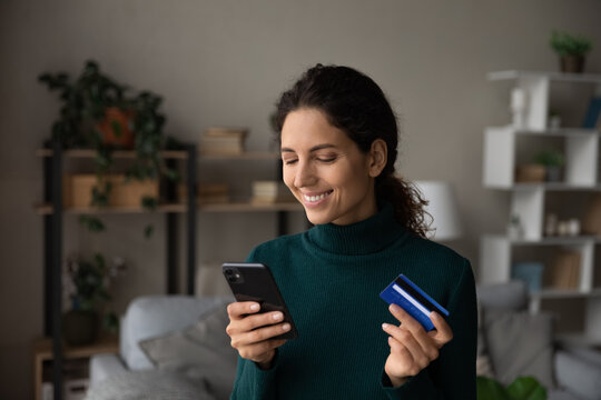 Happy Young Latino Woman Shopping Online On Smartphone Gadget With Credit Debit Card From Home. Smiling Millennial Hispanic Female Make Payment On Cellphone Use Secure Banking App On Device.