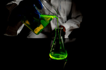 A research scientist experimenting with a green fluorescent droplets in a glass conical flask in...