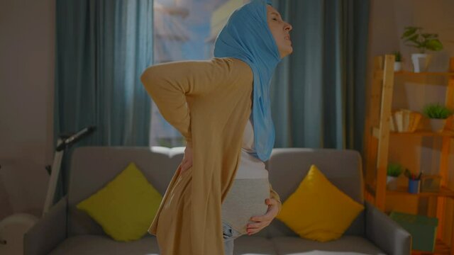 pregnant Muslim young woman in a headscarf feels pain and discomfort in the lower back and back