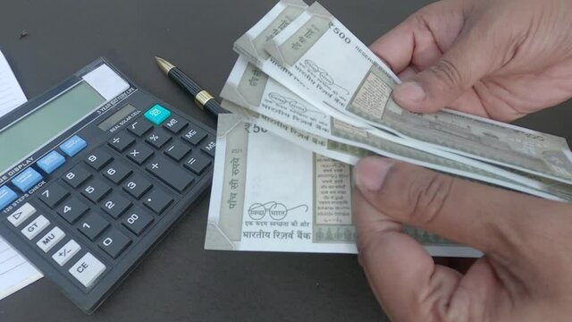 Human hand counting new 500 rupee indian currency note against a calculator and a pen placed on table. High angle view. Close up. Banking Business Finance Background.