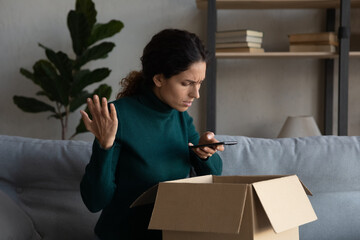 Unhappy young Latino woman unpack box get wrong order shopping online on cellphone. Upset Hispanic...
