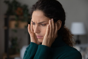 Unhappy young Latino woman touch head suffer from migraine headache at home. Unwell sick Hispanic...