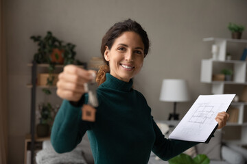 Portrait of smiling Latin female real estate agent show home keys consider architectural plan. Happy Hispanic realtor or broker offer suggest good house or apartment sale deal. Rent, mortgage concept.