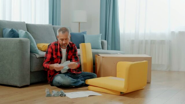 A man in his living room at home unpacks fittings for assembling upholstered furniture.