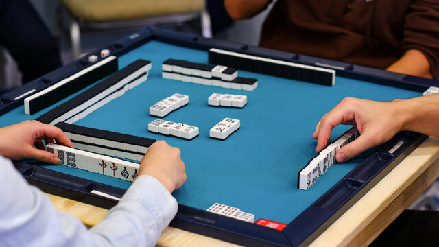 A mahjong table with an active game and the hands of the participants in the game. An ancient Asian game called Mahjong as a way to relax and have fun.