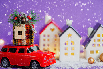 Red retro car on snow carries gift box with home key with keychain cottage on roof past houses with...