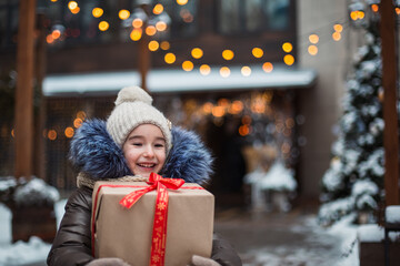 Portrait of joyful girl with a gift box for Christmas on a city street in winter with snow on a...
