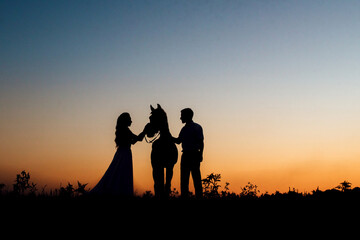 Silhouettes of a bride in a white dress and a groom in a white shirt on a walk