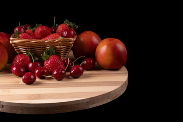 Basket with strawberries and cherries and nectarines. Bamboo board. black background. Space for text.