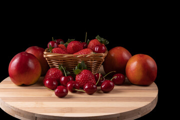 Basket with strawberries and cherries and nectarines. Bamboo board. black background. Space for text.