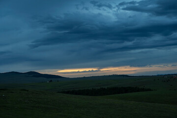 Dramatic sunset behind the mountain. Cloudy sky against the yellow  orange sun. Cloudy sky covering mountain or hill.