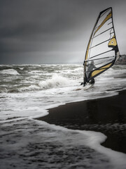 wind surfer with sail on the beach entries into water at storm sea