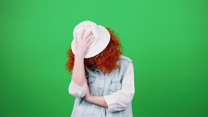 Young boring redhead woman rejecting bad idea, rolling up eyes and covering face with panama hat, posing to camera