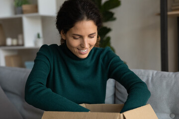 Happy young Hispanic woman feel excited unpack box with internet order shopping online from home. Smiling millennial Latino female buyer or client open unbox package. Good delivery concept.