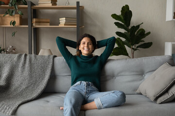 Portrait of smiling young Latino woman relax on couch in living room breathe fresh condition...