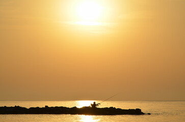 A fisherman in the morning on the seashore catches fish with a line. sunrise in calm and good weather. hobby for fishing and recreation. Background