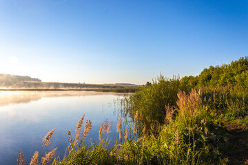 Landscape of lake in mist with sun glow at sunrise